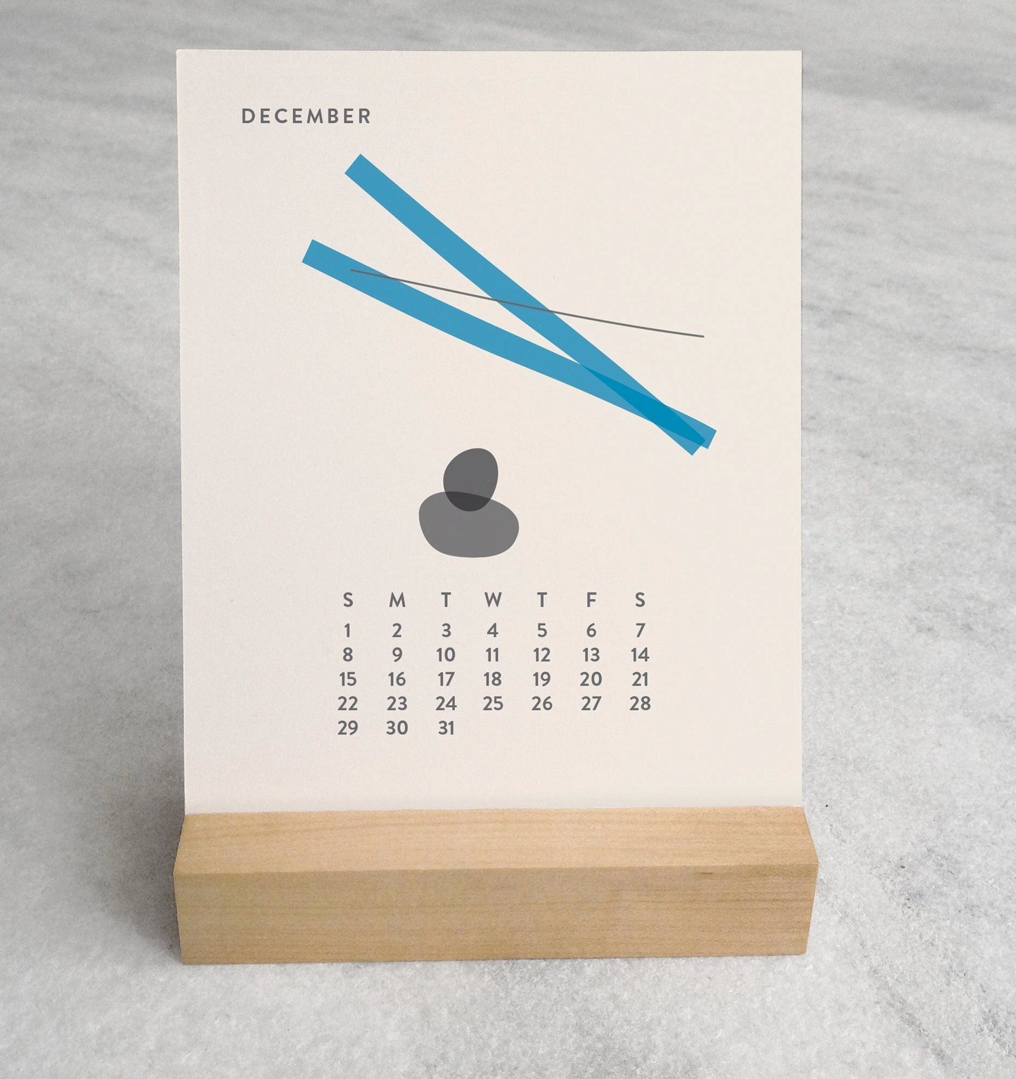 Close-up of the 2025 Desk Calendar December month with a unique monthly design visible on a 4.25" x 5.5" card. The calendar is positioned on a sturdy maple wood stand, emphasizing the quality craftsmanship. The calendar’s compact size is evident as it sits neatly on a small office desk.