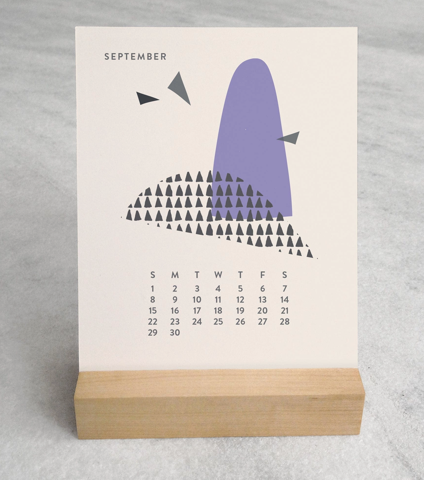 Close-up of the 2025 Desk Calendar September month with a unique monthly design visible on a 4.25" x 5.5" card. The calendar is positioned on a sturdy maple wood stand, emphasizing the quality craftsmanship. The calendar’s compact size is evident as it sits neatly on a small office desk.