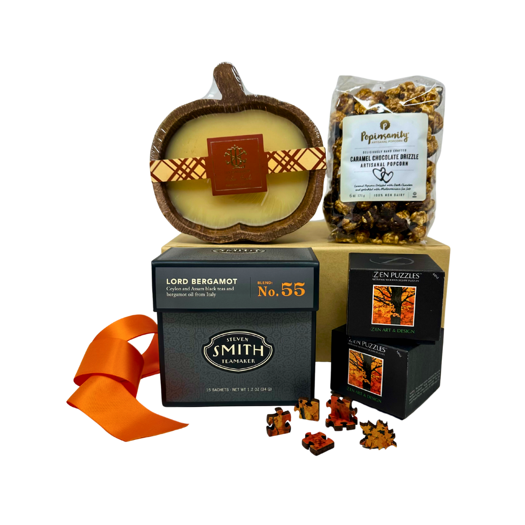 Gift set with Lord Bergamot tea, pumpkin dough bowl candle, caramel and chocolate popcorn and wooden puzzle of fall colored orange maple tree leaves with puzzle pieces on a white background