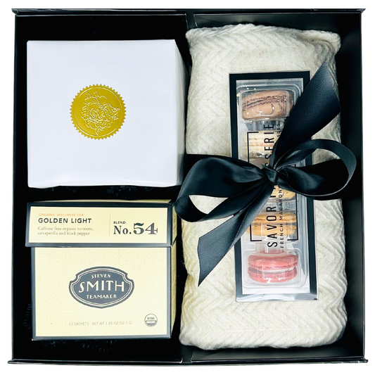 Stunning gift box with a gray cashmere blanket, box of 5 French macarons, golden light tea box and a candle.