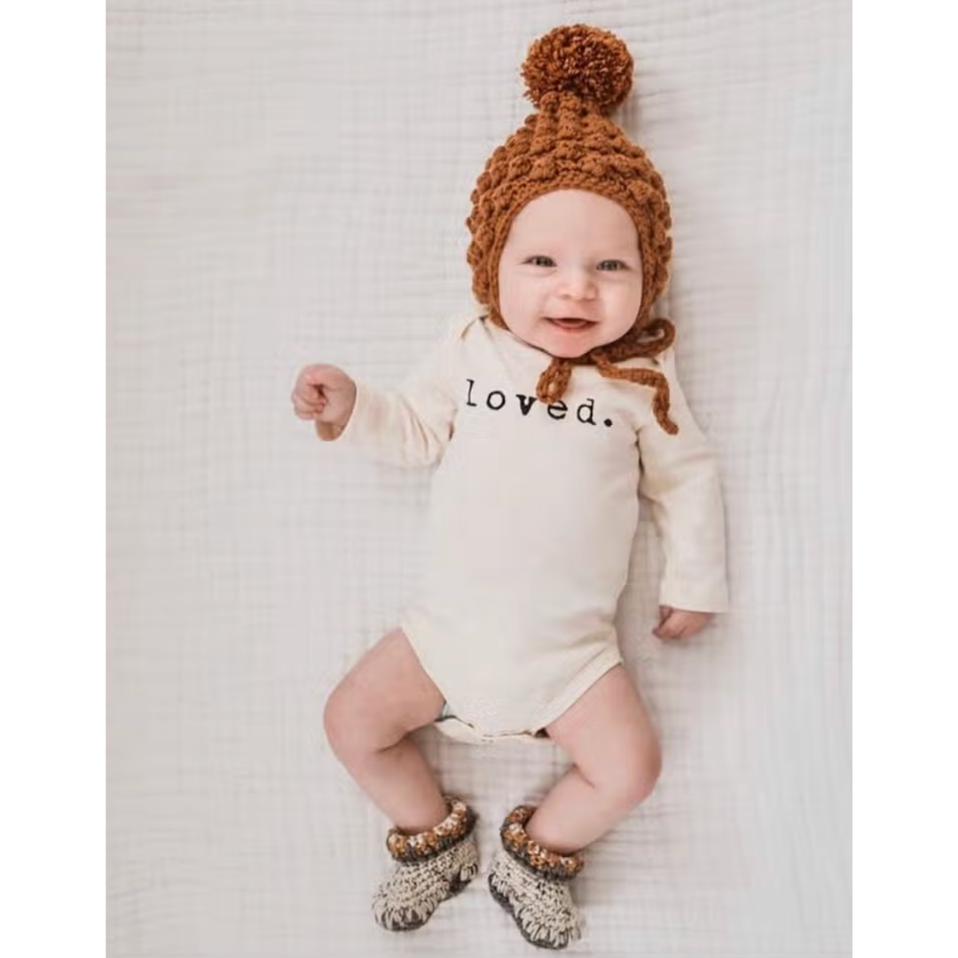Natural cream baby bodysuit crafted from organic cotton, adorned with 'Loved' in black.