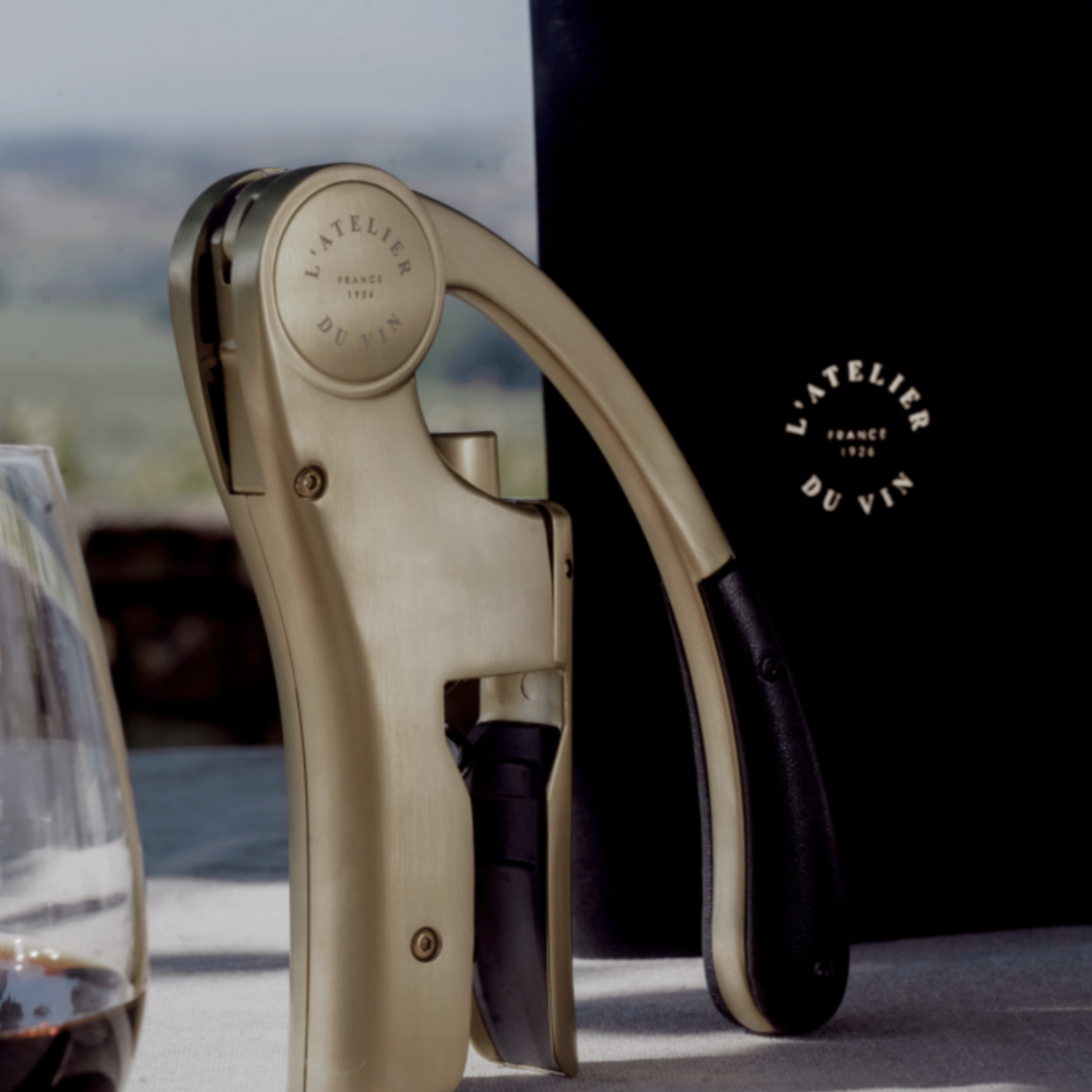 Wine opener by L'Atelier du Vin amidst vineyard scenery.