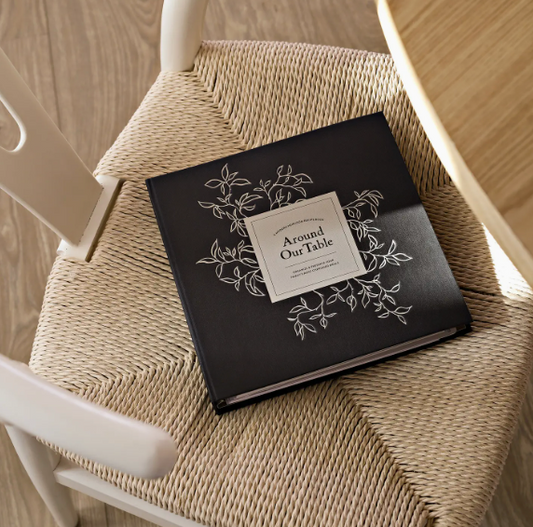 "Around Our Table" recipe book with 138 pages to record family recipes, organized by food category. Includes 20 recipe cards, plastic sleeves for extra recipes, and a durable, wipeable hardcover. Perfect for preserving family meals and memories.