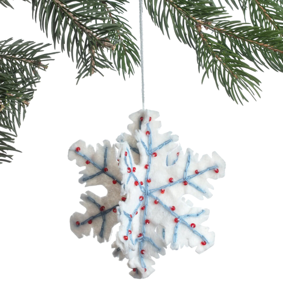 A white felt snowflake ornament adorned with red beading and blue accents. The snowflake has intricate cut-out patterns and is embellished with small red beads around its edges and blue accents in the center, creating a festive and decorative look.