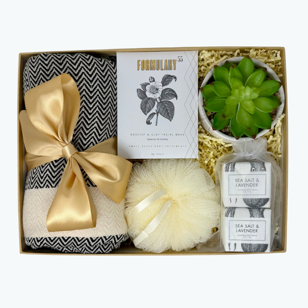 Gift set with bath items including a towel, faux succulent, facial mask, loofah and bath salts  in a box.