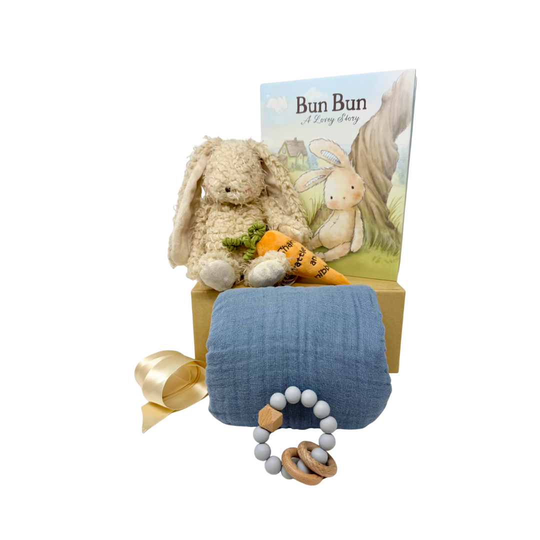 Baby gift set with plush bunny, plush orange carrot, book, beechwood teether, and blue blanket on a white background.