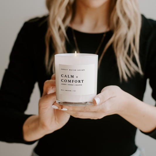 Woman in black shirt holding candle in white glass.