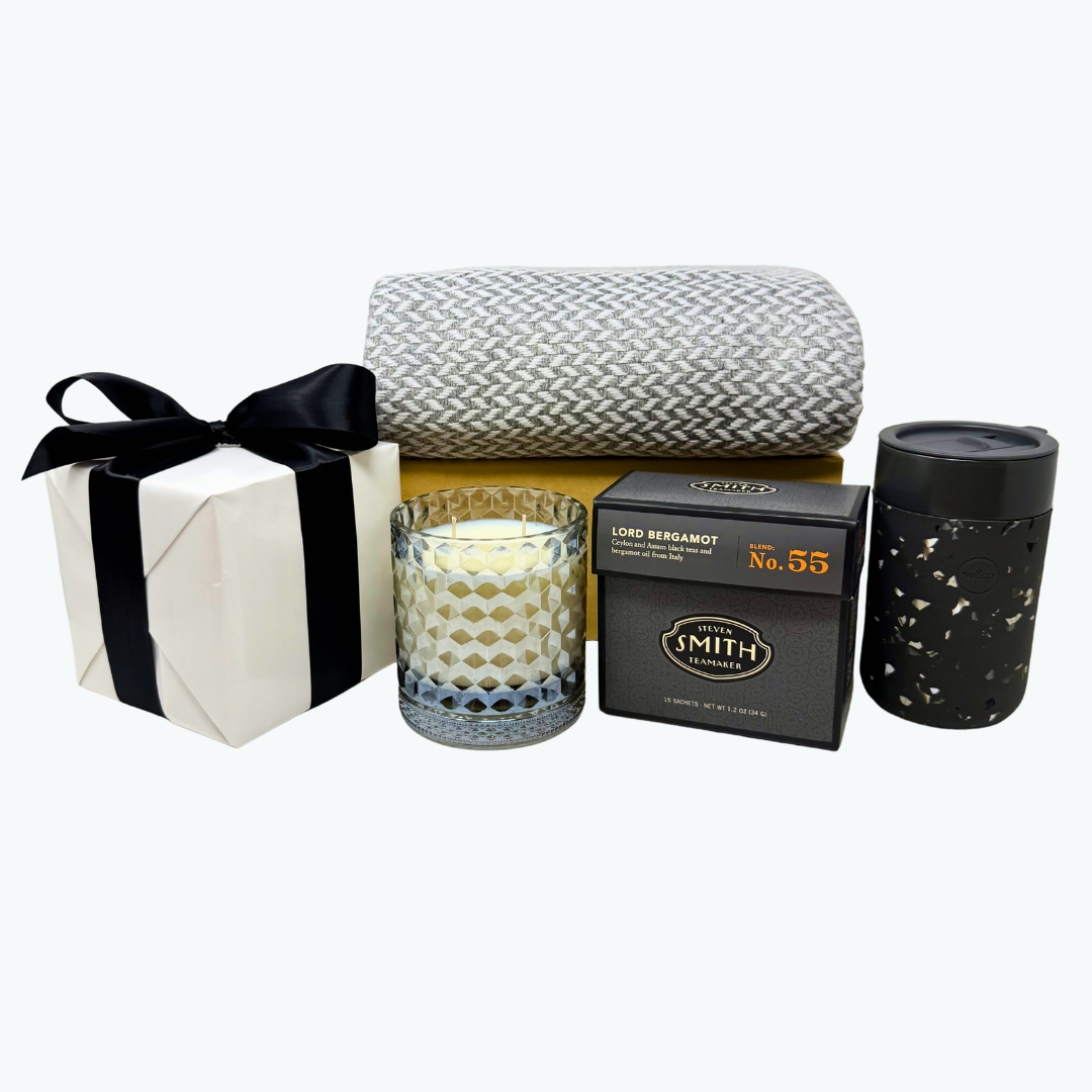 Gift set with grey glass candle, black box of Lord Bergamot tea, grey and white herringbone cashmere blanket and other items on a white background.