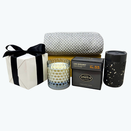 Gift set with grey glass candle, black box of Lord Bergamot tea, grey and white herringbone cashmere blanket and other items on a white background.