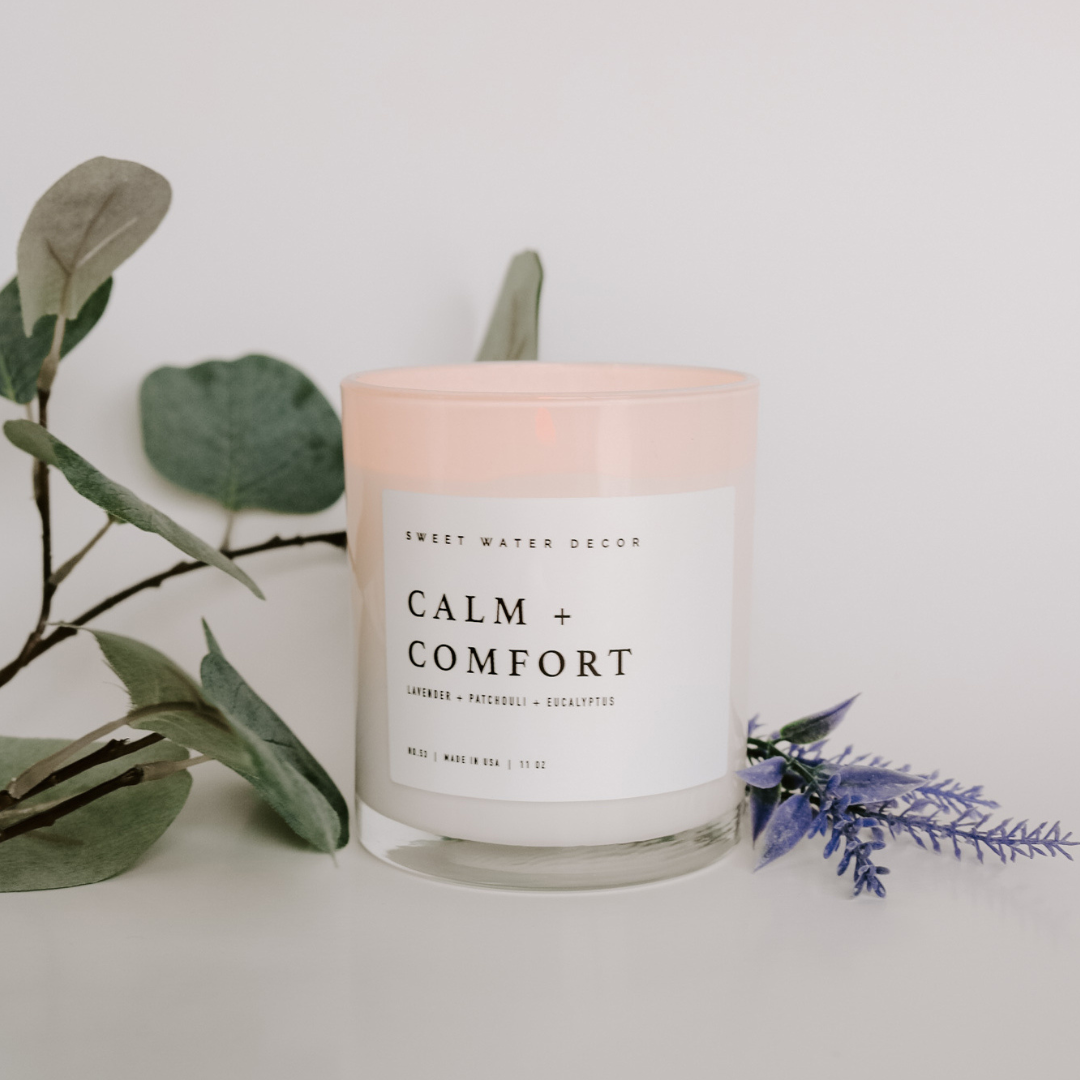 Candle on white background with grren plant in background.