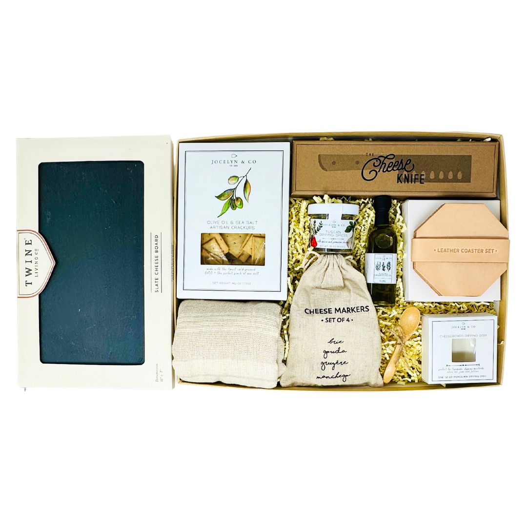 Cheese Please Charcuterie Board Gift Box with a slate board, olive oil, dipping spices, crackers, cheese markers, leather coasters, and a cheese knife, offering a complete gourmet experience for any occasion.