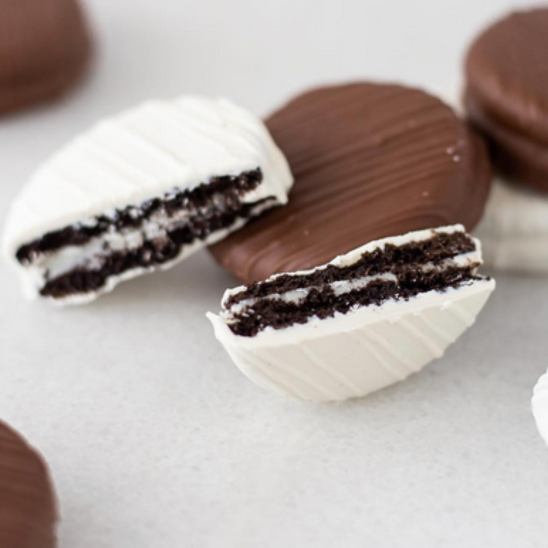 Milk and white chocolate-covered cookies. The cookies are high-quality Oreo cookies coated in a rich blend of milk and white chocolate. The elegant packaging highlights the artisanal quality and festive decoration of the cookies, which are crafted by Maggie Lyon Chocolatiers, a family-owned confectionery company. Ideal for gifting or personal enjoyment, these cookies combine traditional craftsmanship with gourmet indulgence.