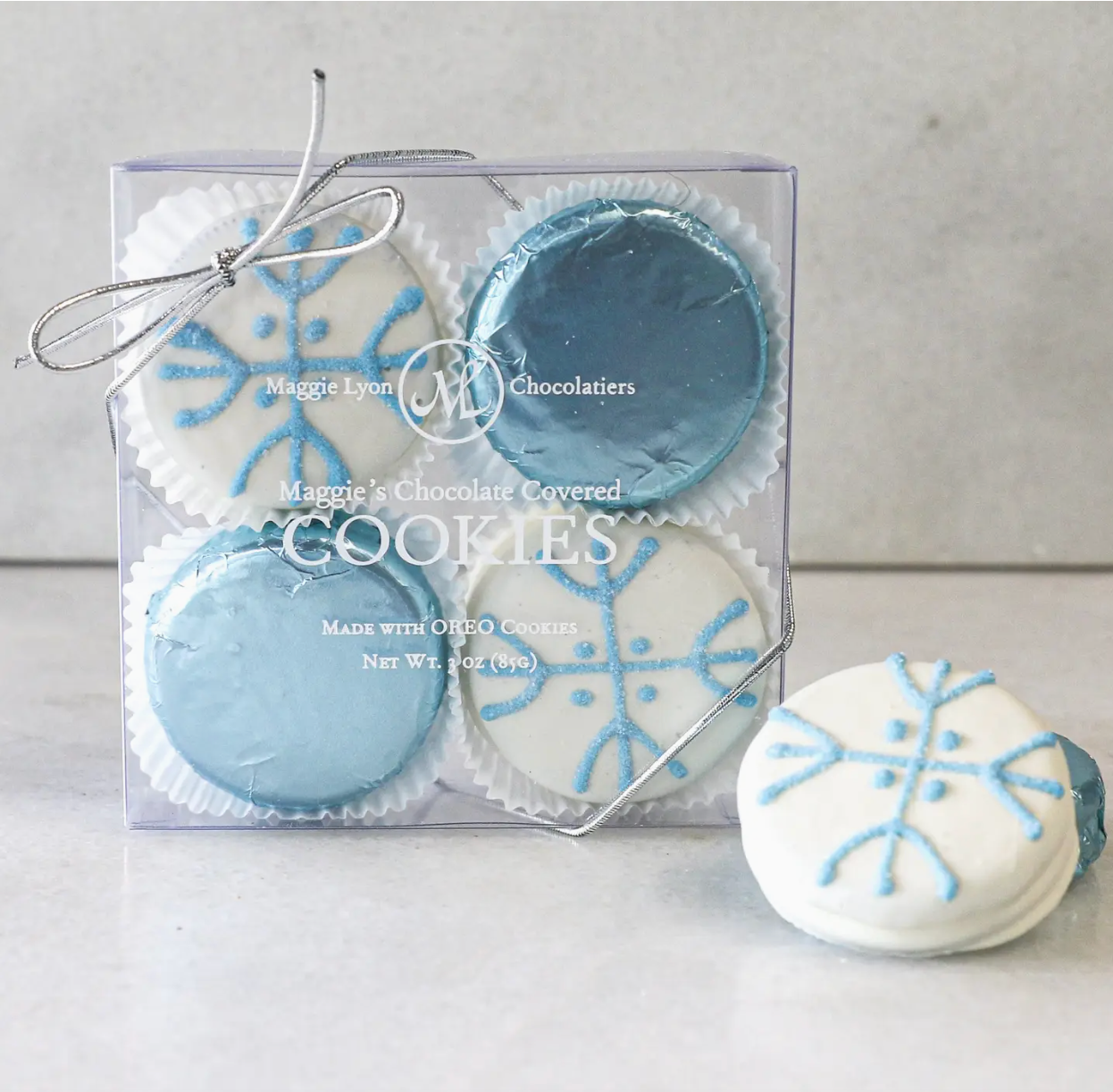 Four Oreo cookies covered in milk and white chocolate, each hand-decorated with a snowflake design. The cookies are beautifully presented, showcasing the intricate snowflake details and shiny chocolate coating.