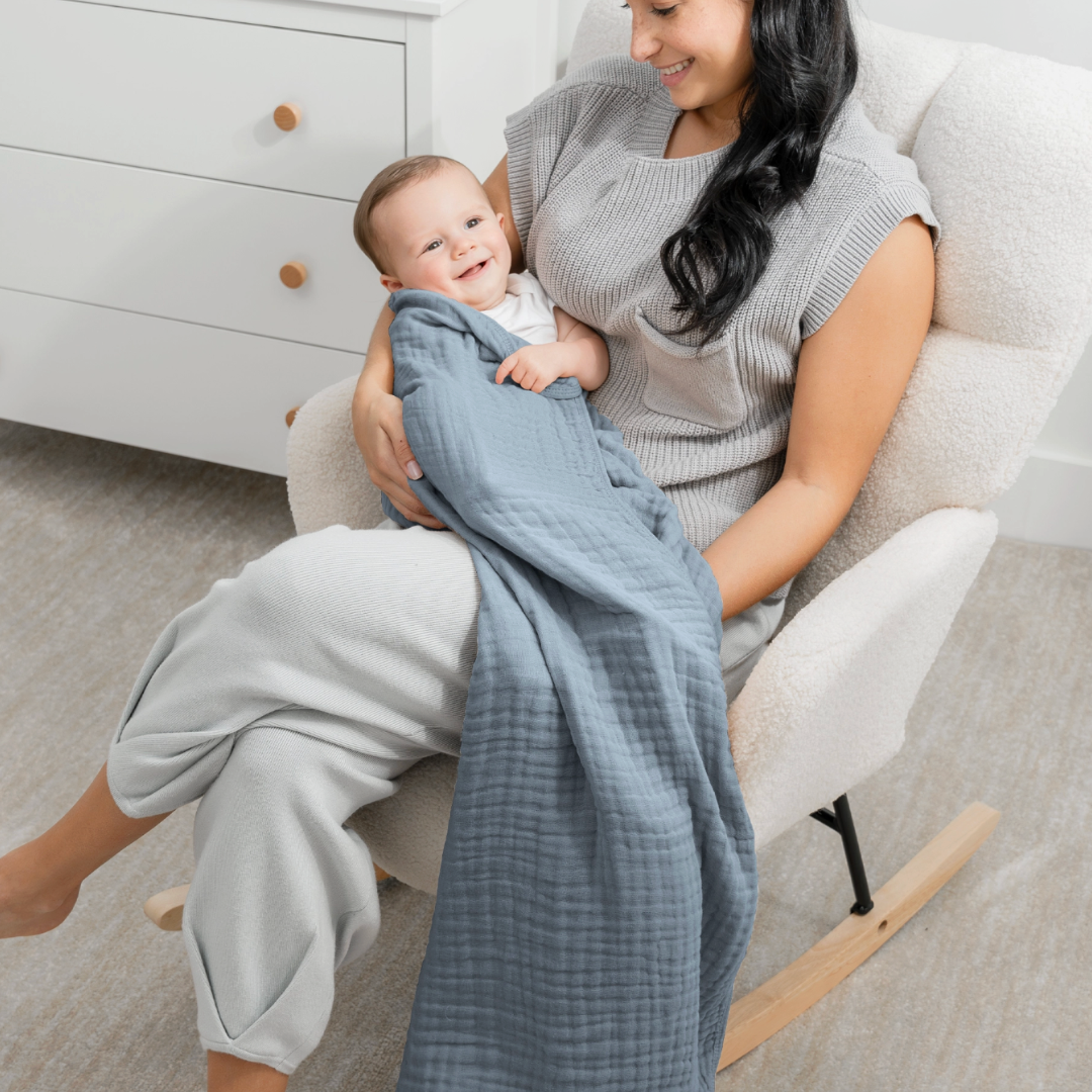 Mom rocking a baby wrapped in a blue muslin baby blanket in a nursery.