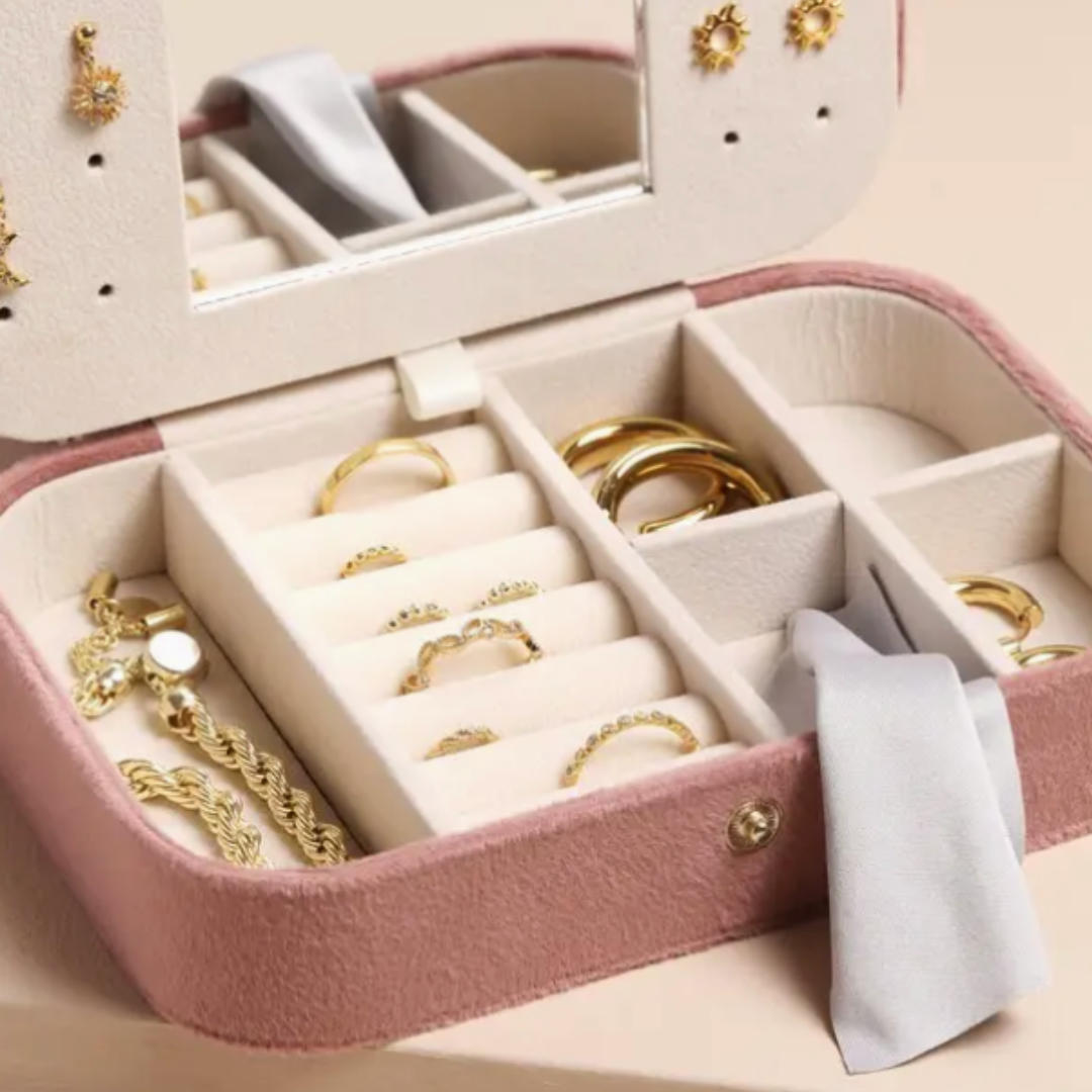 Compact rose pink travel jewelry box made of soft velvet, featuring multiple compartments, a mirror, and a silky polishing cloth for organizing accessories.