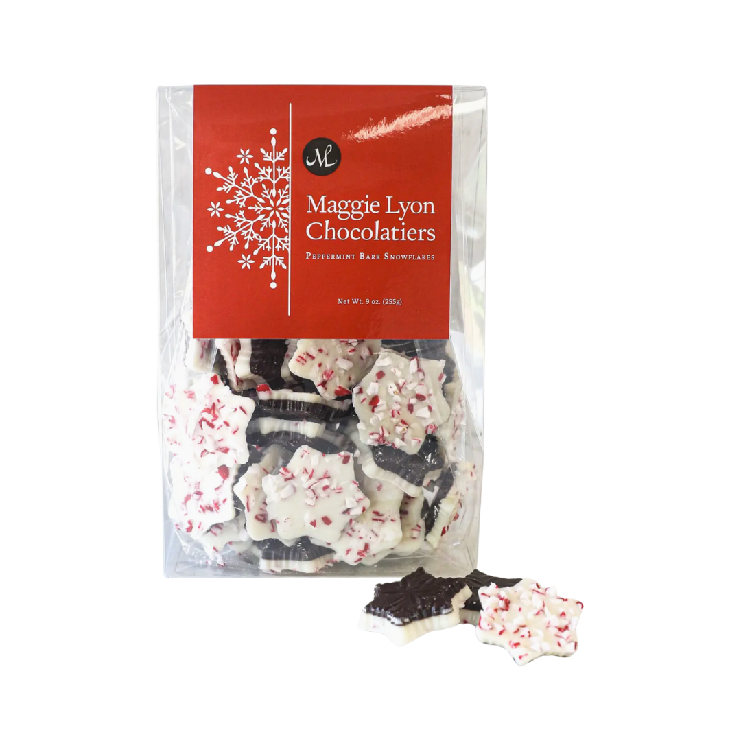 A close-up of Maggie Lyon Chocolatiers Mini Snowflake-shaped Peppermint Bark, featuring a combination of dark and white chocolate with peppermint crunch. The bark is delicately layered, with festive colors and a shimmering finish. The packaging is shown, which is a 10.56 oz box measuring 4.5 x 2 x 7 inches, perfect for gifting or personal enjoyment during the holiday season.