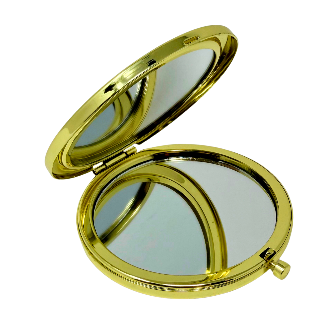 An oval gold compact mirror shown open against a plain white background, with a polished gold frame and mirrored interior.