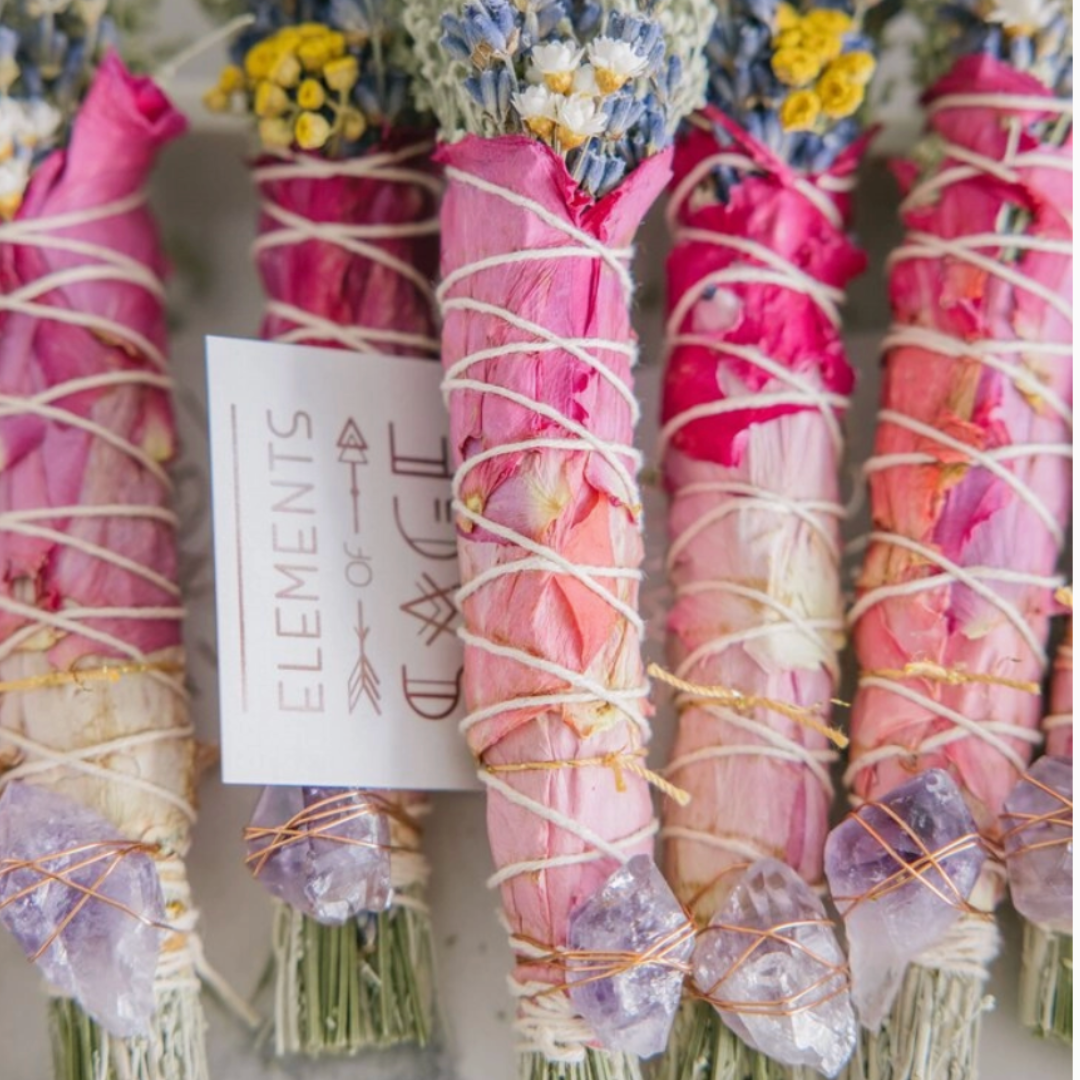 Handcrafted Floral Sage Bundle with a mix of lavender, rose petals, and other dried flowers, complemented by a genuine crystal. The bundle is shown in a serene setting, highlighting its natural and rejuvenating qualities.