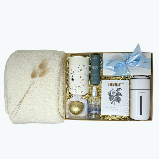 Gift box containing a blanket, mug, bottle, and other items on a white background.