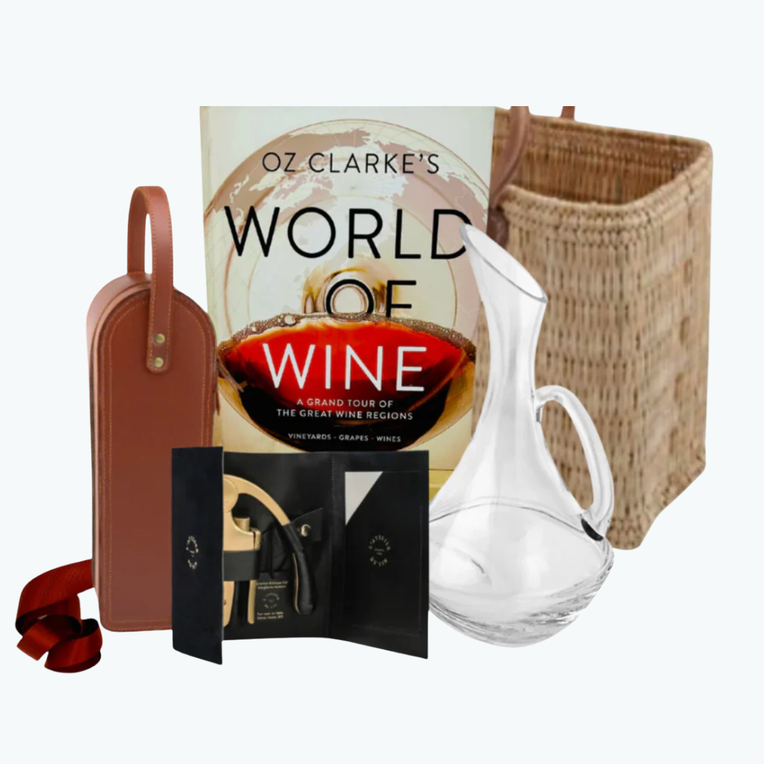 Coffee table book with a hand blown glass decanter, basket tote with leather handles, leather bottle carrier, corkscrew and other items on a white background.