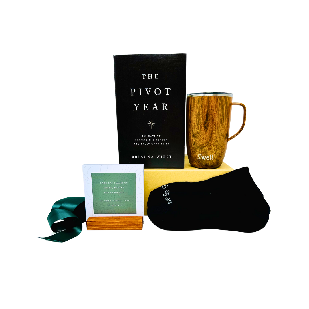 Curated gift box containing a book called The Pivot Year, a wooden grain reusable tumbler by Swell, Be Great black ankle socks and a wooden stand with motivational cards.