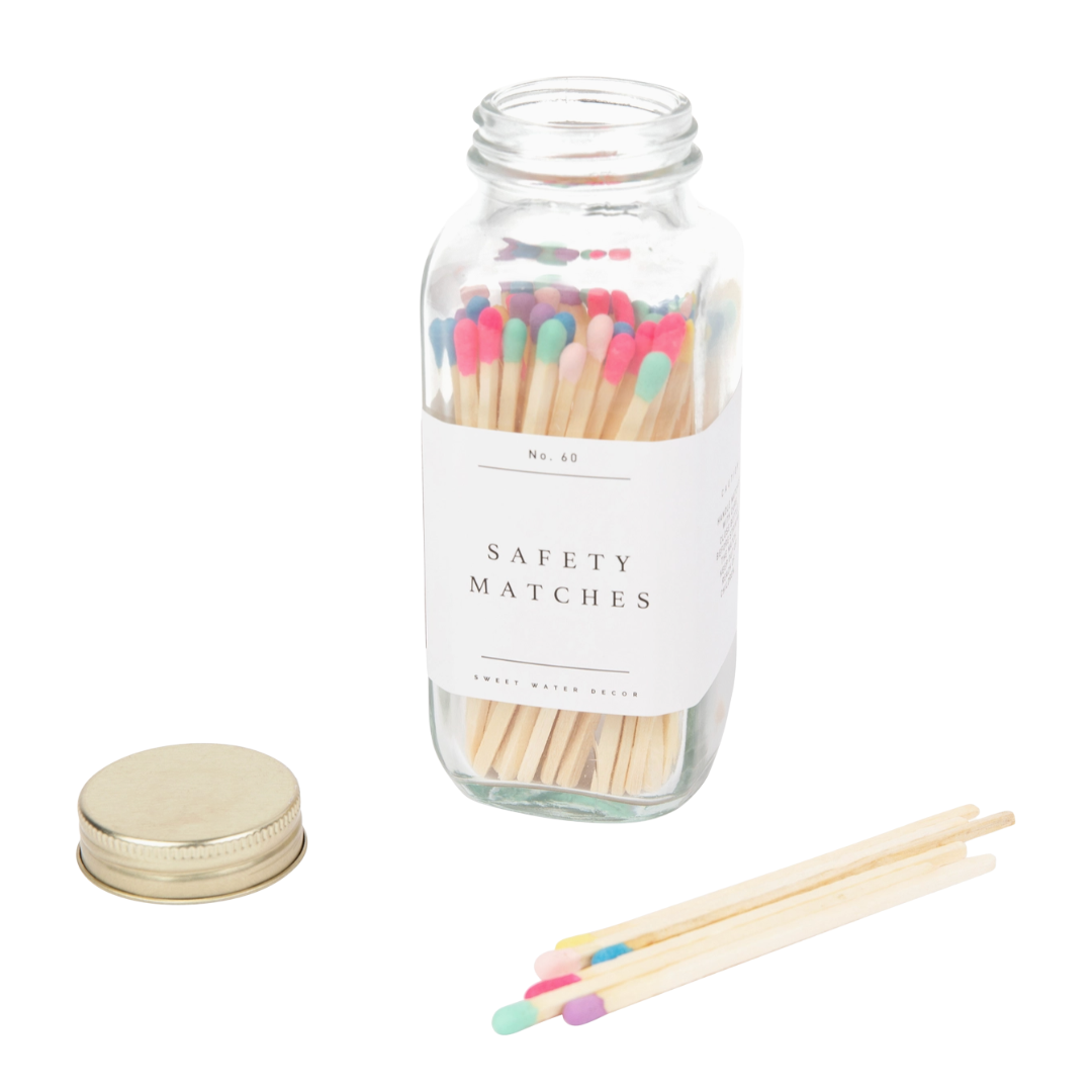 Glass jar of wooden safety matches with colorful heads on a white background. Some of the tips are pink, purple, mint green, yellow, bright blue and peach colored.