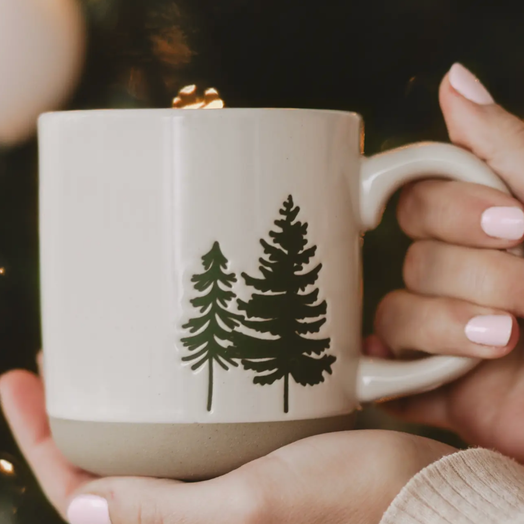 Person holding a mug with tree design against a blurred background.