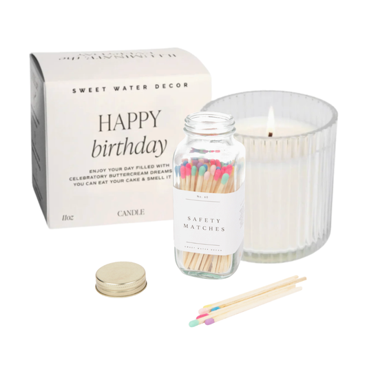 A Happy Birthday candle gift set by Sweet Water Decor, featuring a white candle in a ribbed glass jar, a glass jar of safety matches with colorful tips, a gold metal lid, and the white product box with 'HAPPY birthday' printed on it.