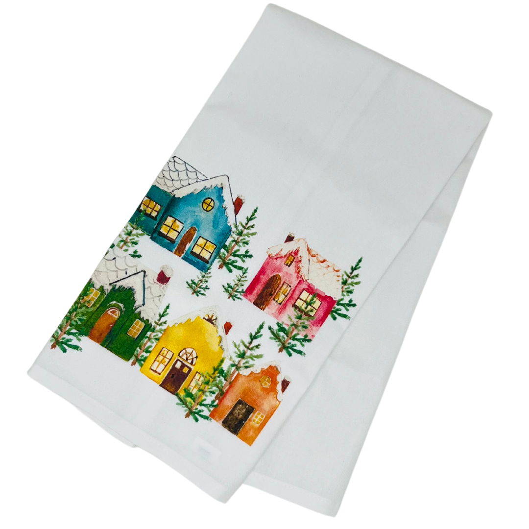 A kitchen towel featuring a charming winter scene with colorful cottages. The design includes snow-covered rooftops and cozy cottages in various bright hues, set against a snowy backdrop. The towel’s festive pattern captures the essence of a cozy winter landscape.