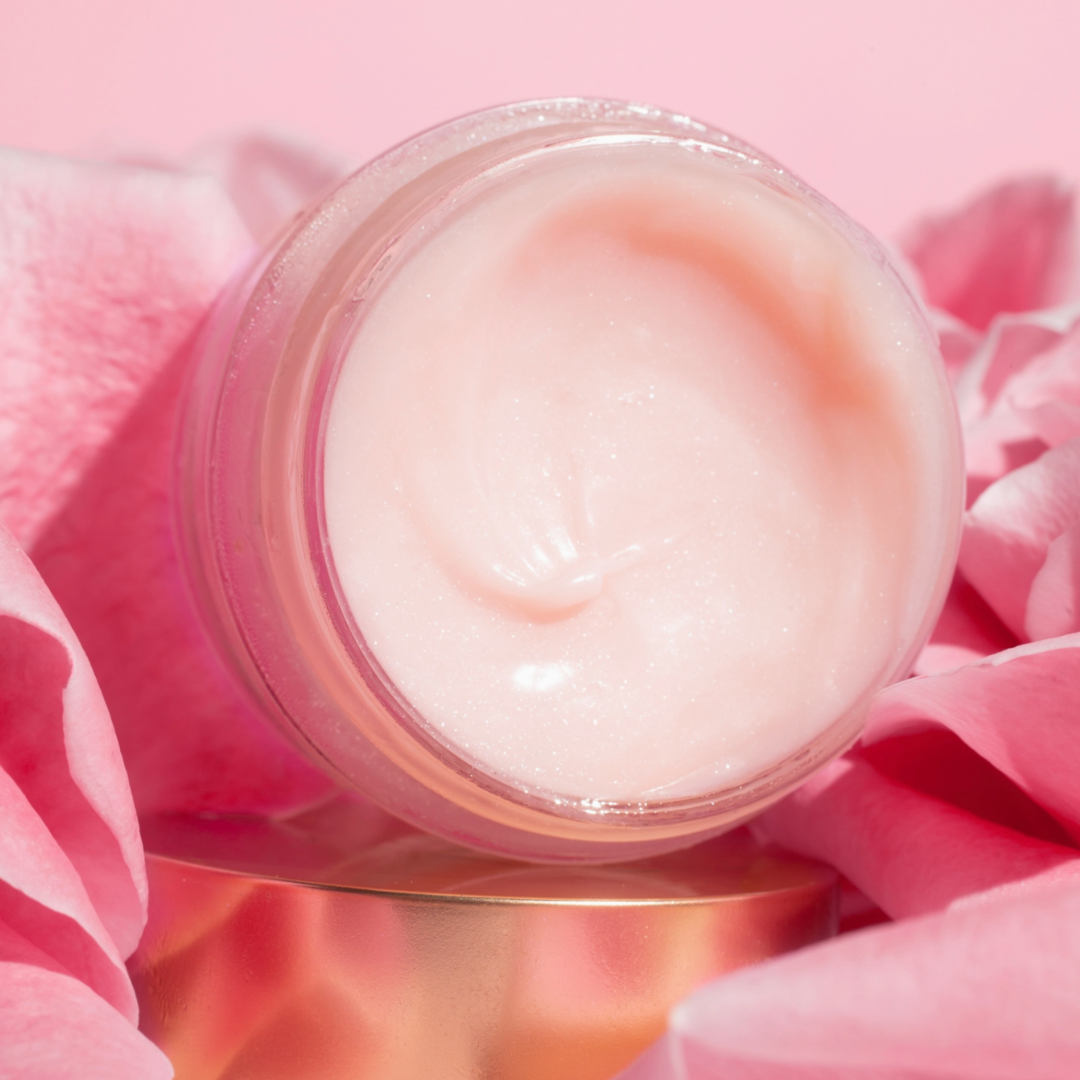 Jar of creamy lip balm on a pink background with pink flowers.
