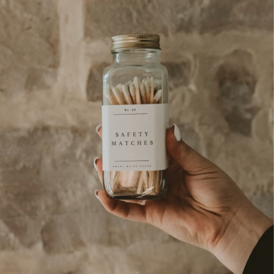 Hand holding a glass jar of safety matches with a stone wall background