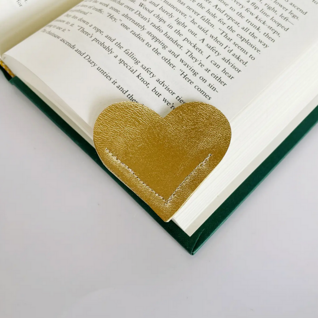 A textured metallic gold heart-shaped book bookmark resting on the pages of an open book.