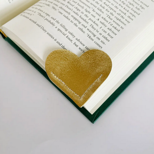 A textured metallic gold heart-shaped book bookmark resting on the pages of an open book.