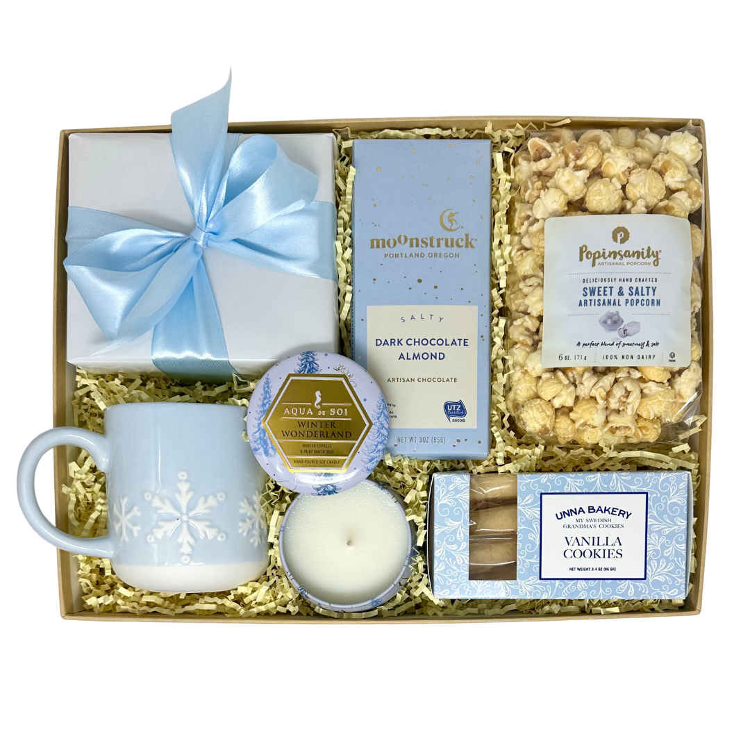 Gift set with popcorn, light blue with white snowflake mug, cookies, and candle and chocolate bar on a white background.