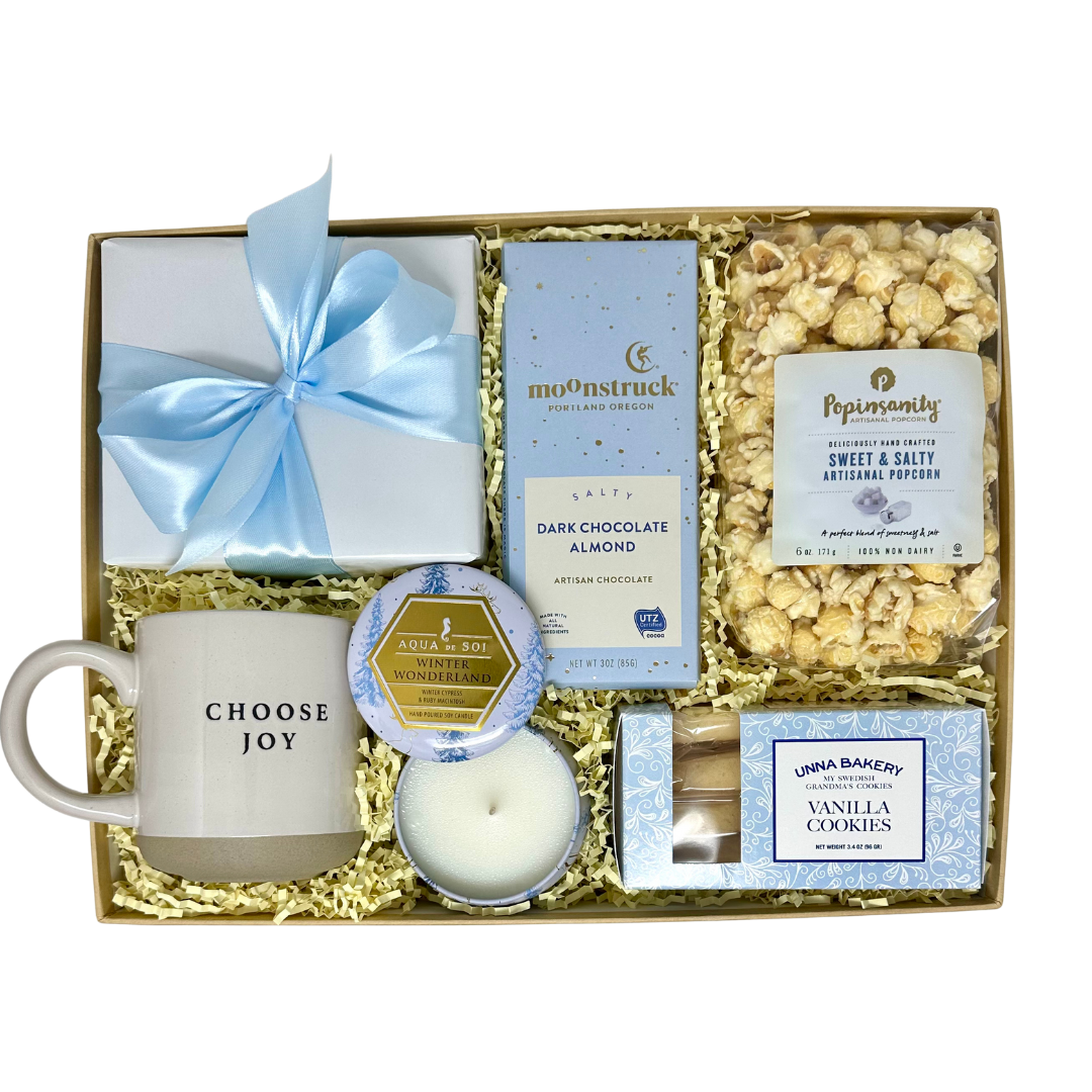 Holiday gift box on a white background with a stoneware mug, vanilla cookies, chocolate bar, popcorn and a candle on a white background.