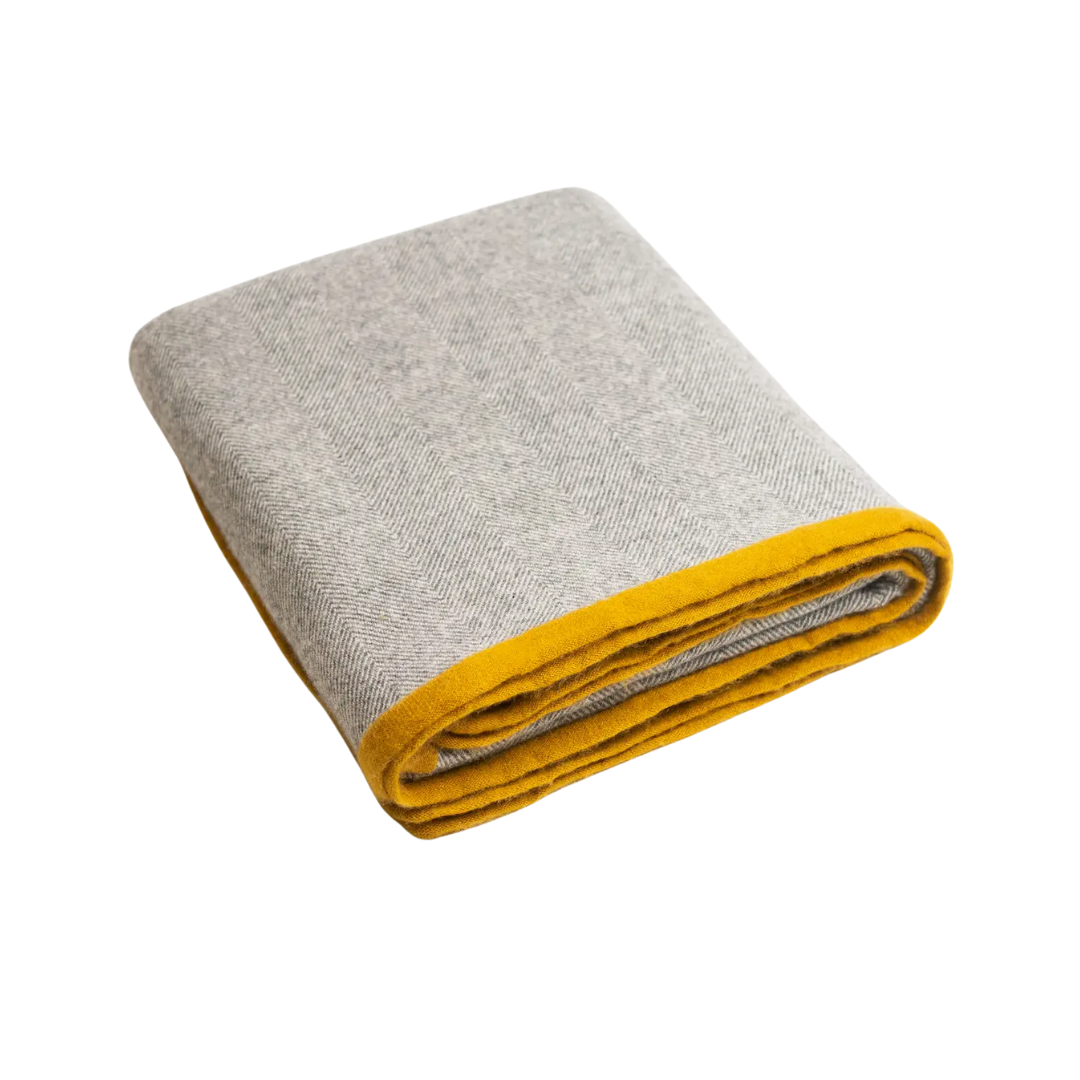 Folded blanket with gray herringbone and yellow trim on a white background.
