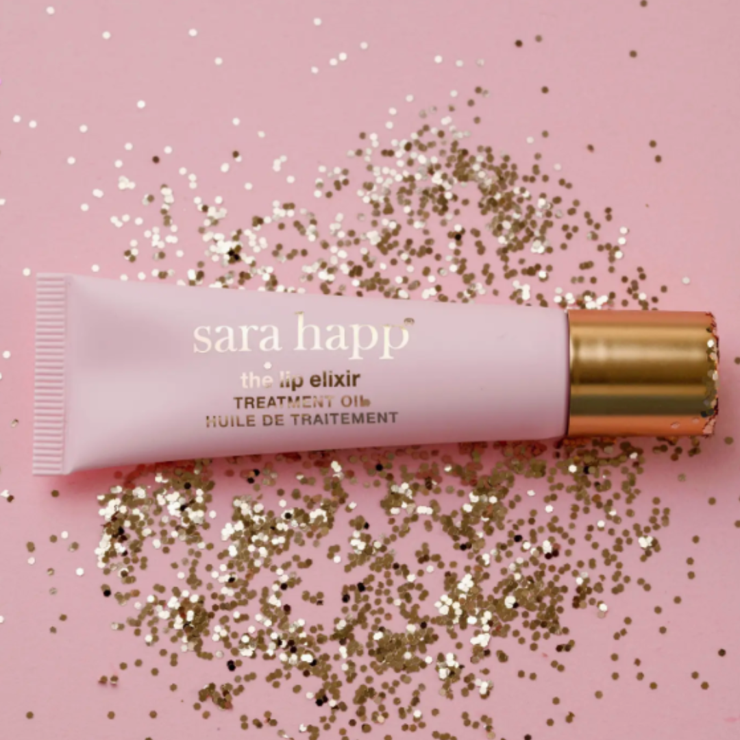 sara happ lip elixir treatment oil on a pink background with gold glitter