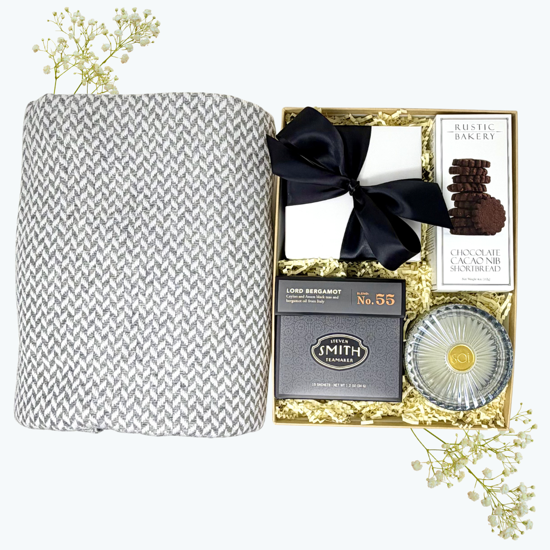 Gift set with cashmere blanket, candle, tea, and other items in a decorative box on a white background.
