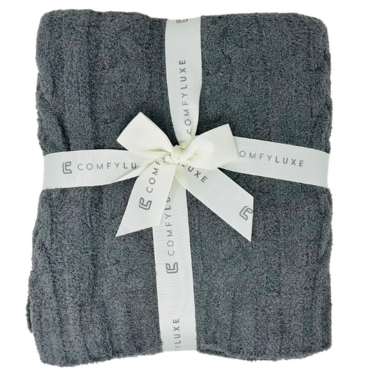 A 50x60 inch charcoal gray throw blanket with a super soft knit texture. The blanket is draped smoothly, showcasing its cozy and plush material with a subtle ribbed pattern. The deep charcoal color adds a touch of elegance and warmth.