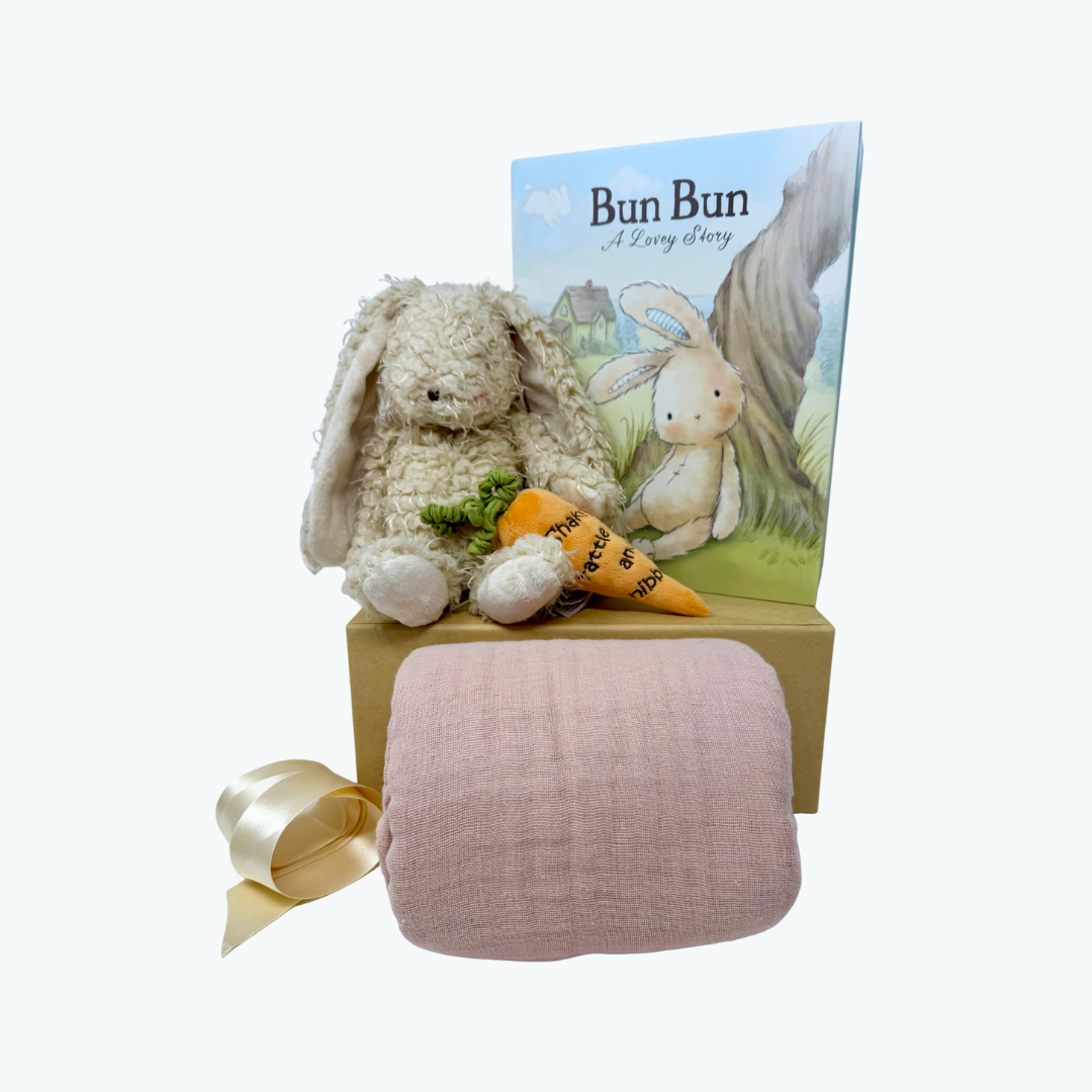 Stuffed bunny toy with a book and pink blanket on a white background.
