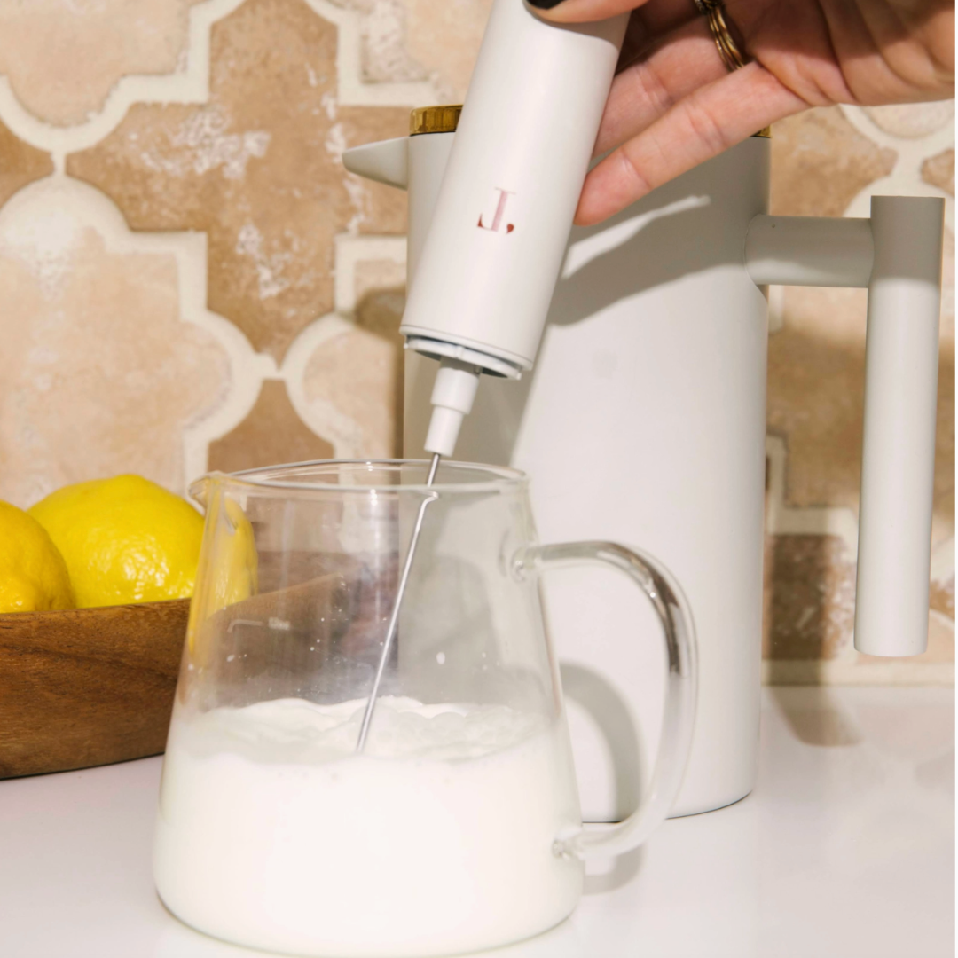 A cream-colored milk frother, featuring a sleek design with a frothing wand and ergonomic handle, ideal for creating frothy milk for coffee drinks.