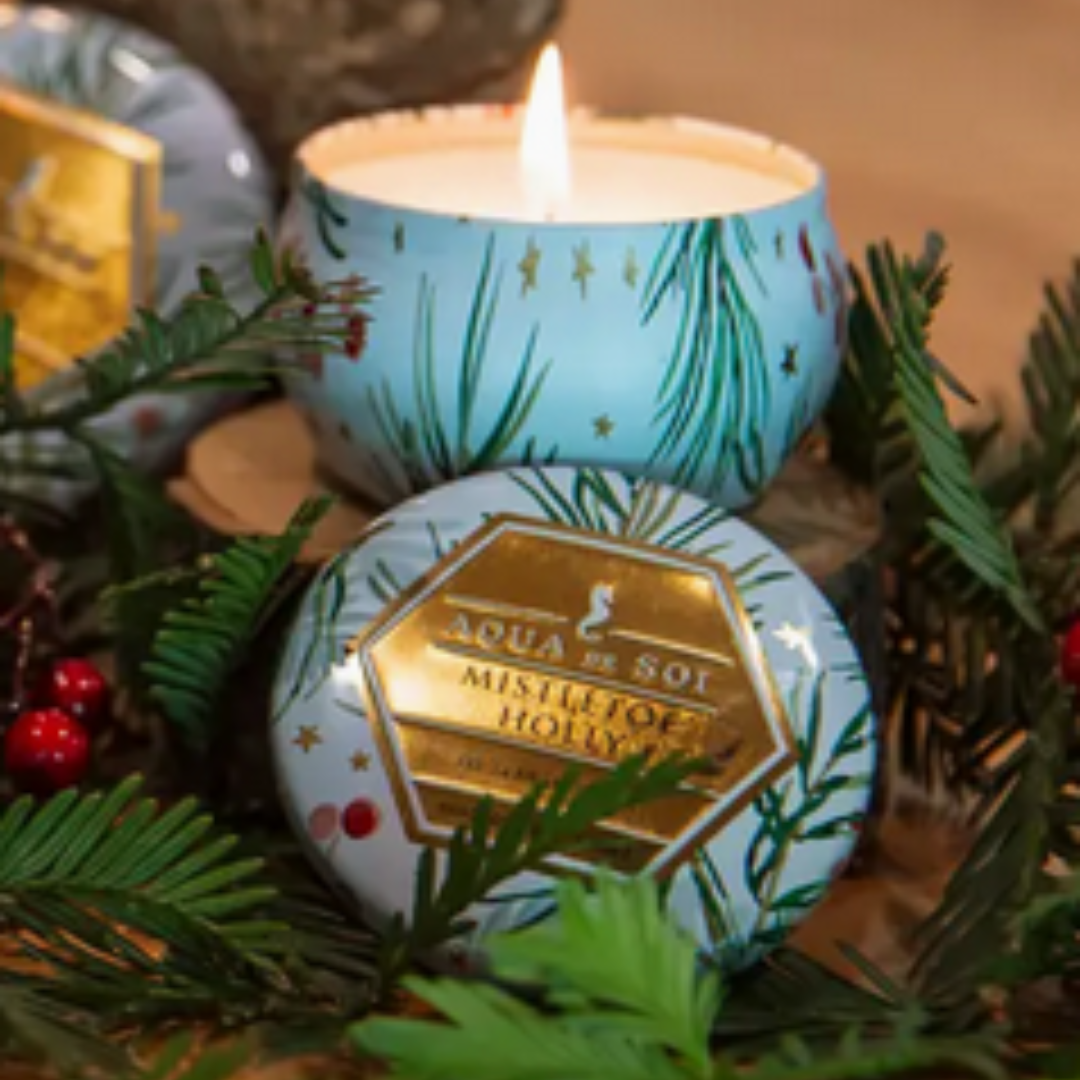 The Mistletoe & Holly Candle from Aqua de Soi, displayed in a glass jar with a cotton lead-free wick. This 4-ounce soy candle is hand-poured using natural ingredients, providing a soot-free burn with a blend of snow-covered Fraser fir, balsam cedar, and a hint of juniper berry.