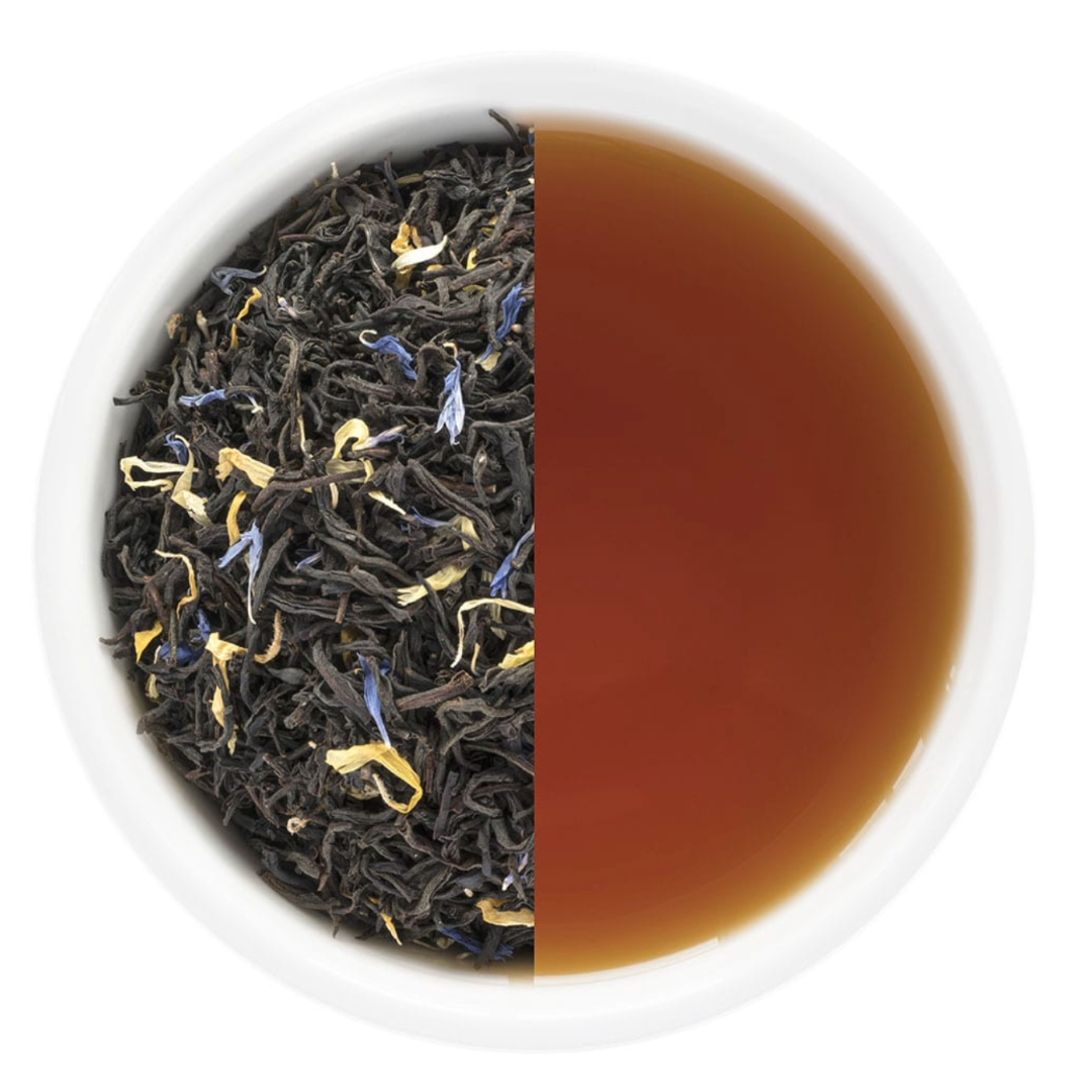 The Monista Tea No.1 French Earl Grey in a festive canister, showcasing the blend's aromatic ingredients, including black tea and colorful cornflower blossoms, set against a backdrop of winter greenery.