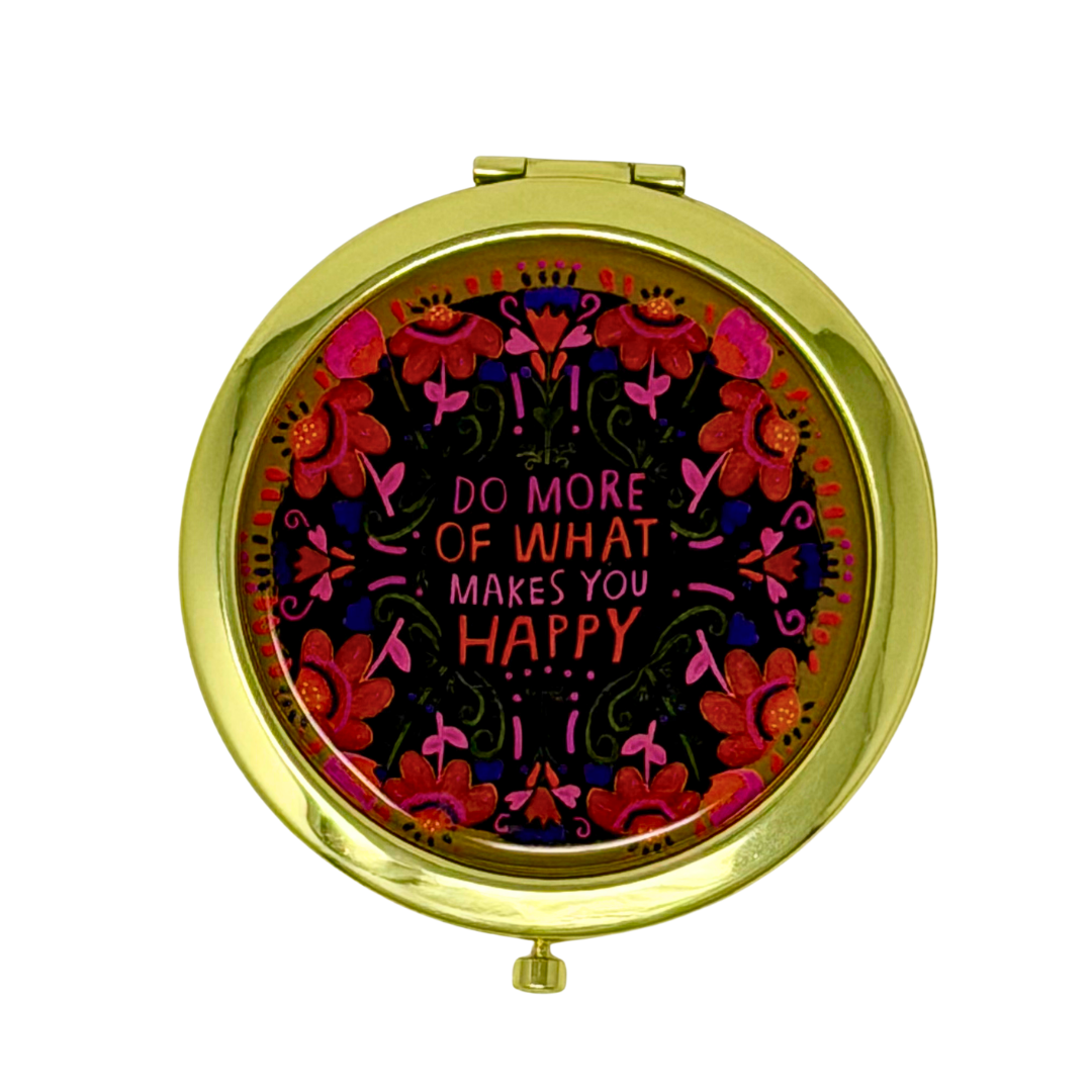A round gold compact mirror with a colorful floral design and the text 'DO MORE OF WHAT MAKES YOU HAPPY' on the front, shown against a plain white background.