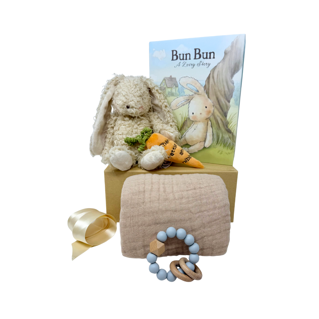 Baby gift set with plush bunny, plush orange carrot, book, sand colored muslin blanket and teether on a white background.