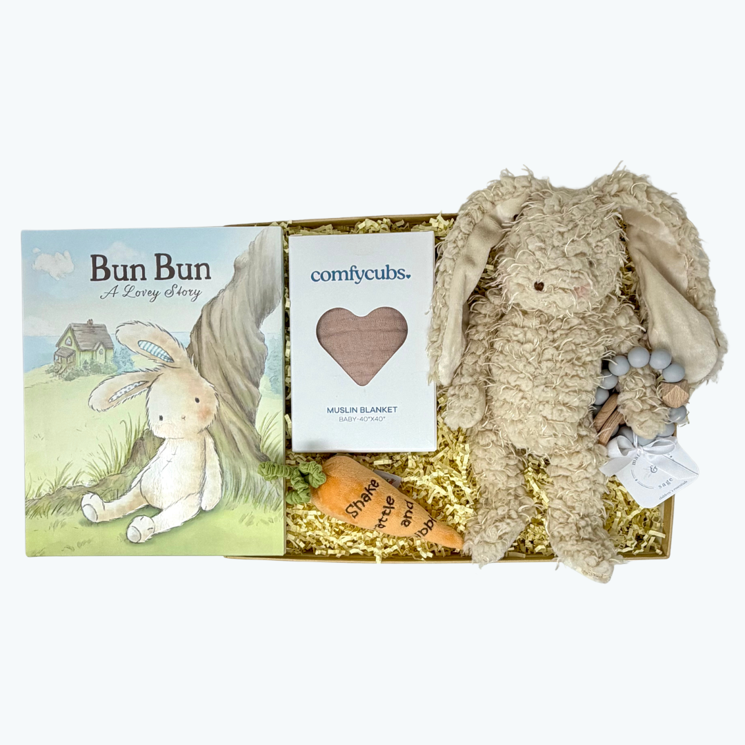 Baby gift set with plush bunny, muslin blanket, carrot rattle, teether, and book on a white background.