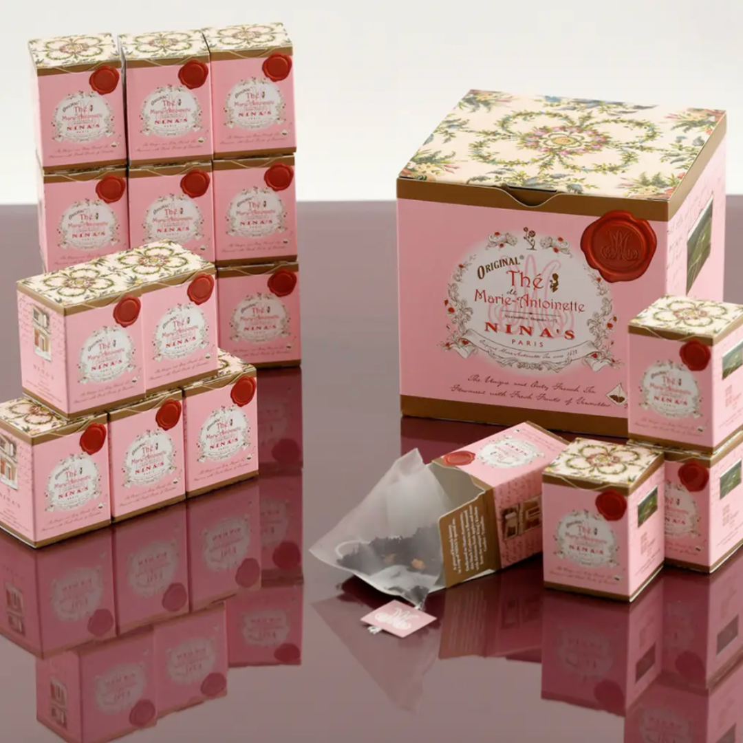 A decorative gift box from Nina’s of Paris featuring 18 mini pink boxes, each containing a single tea bag of Marie-Antoinette tea. The box displays an elegant design and contains a blend of Ceylon tea with rose petals, apple essence, and rose from Versailles. Made in France, this tea offers a luxurious and comforting experience, perfect for someone battling breast cancer. The packaging reflects a rich heritage and commitment to high-quality, eco-responsible tea production.