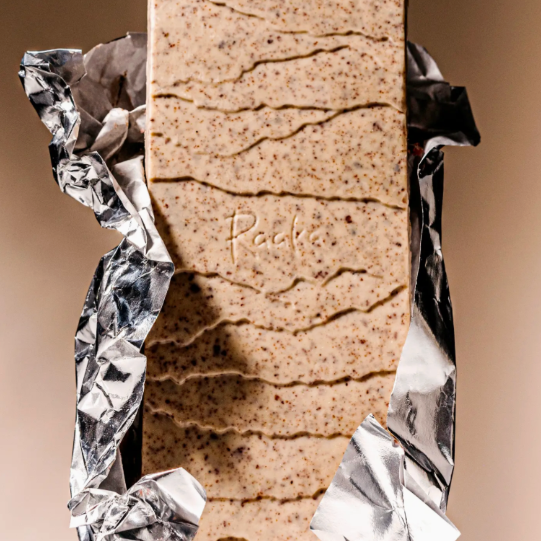 Opened packaging of Raaka's Cookies and Cream White Chocolate Bar on beige background.