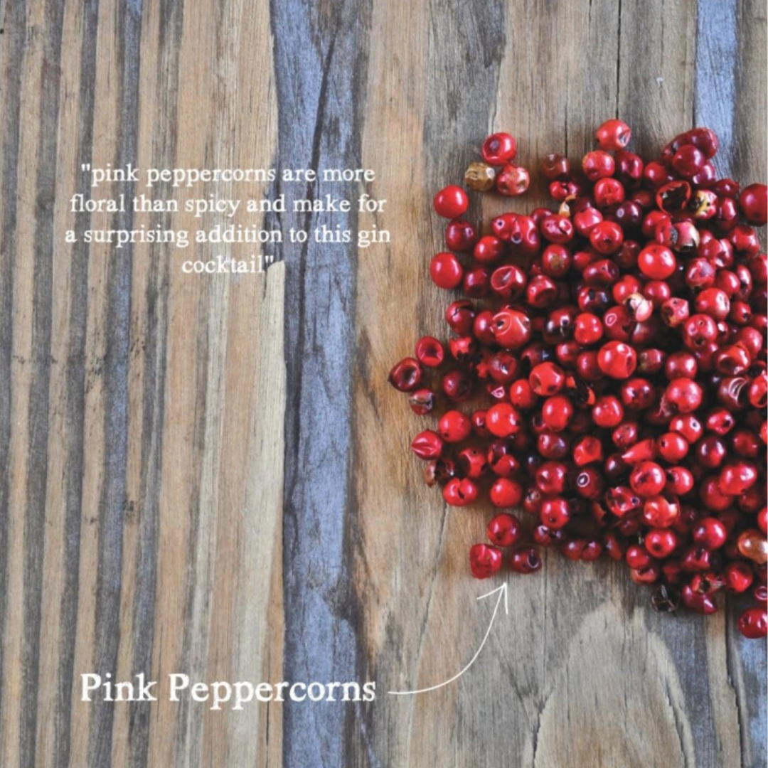 Soft cover recipe book offering tips for mixing cocktails at home including recipes using pink peppercorns. A large pile of round pink peppercorns are displayed on a wooden table.