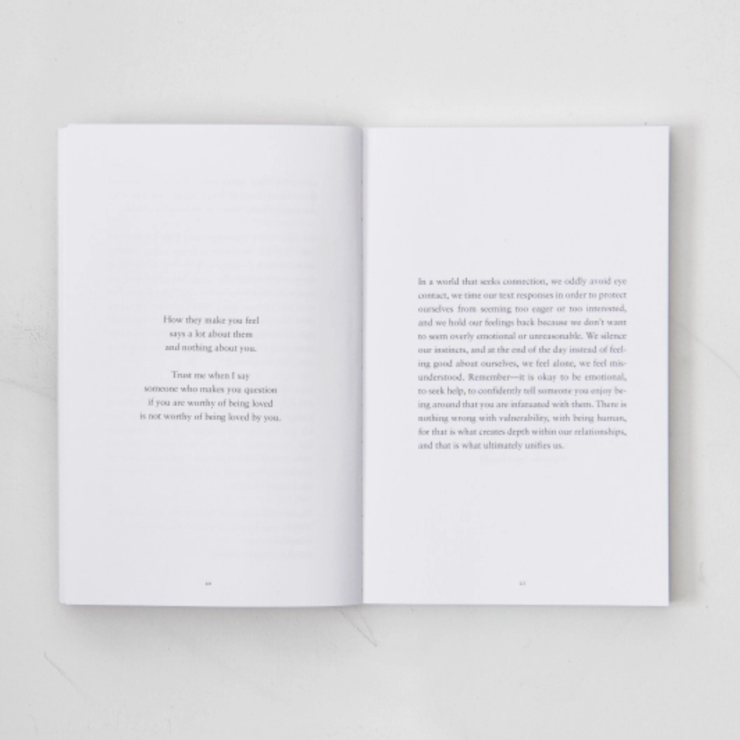 An open book with two printed pages laid flat on a light gray surface. The pages contain black serif text, with the left page featuring a short poem and the right page longer prose text.